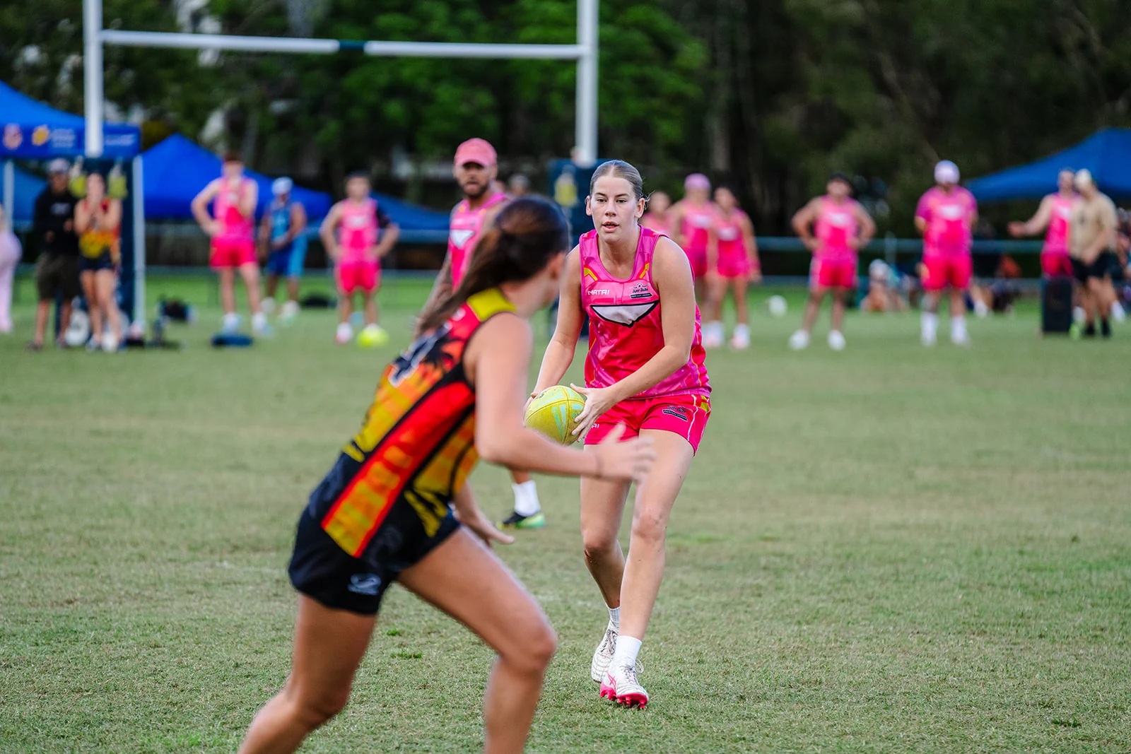 A woman in pink watches an approaching defender with the ball held ready.