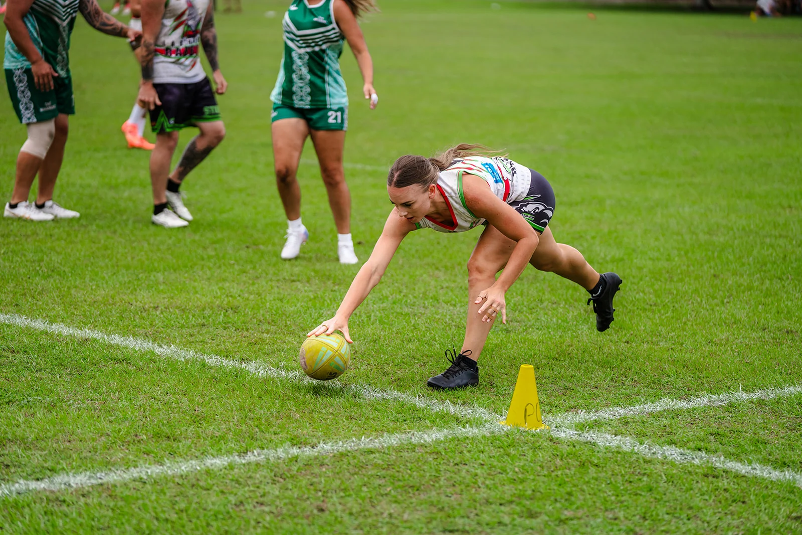 A woman lowers the ball beside a sideline cone with her eyes on the turf.