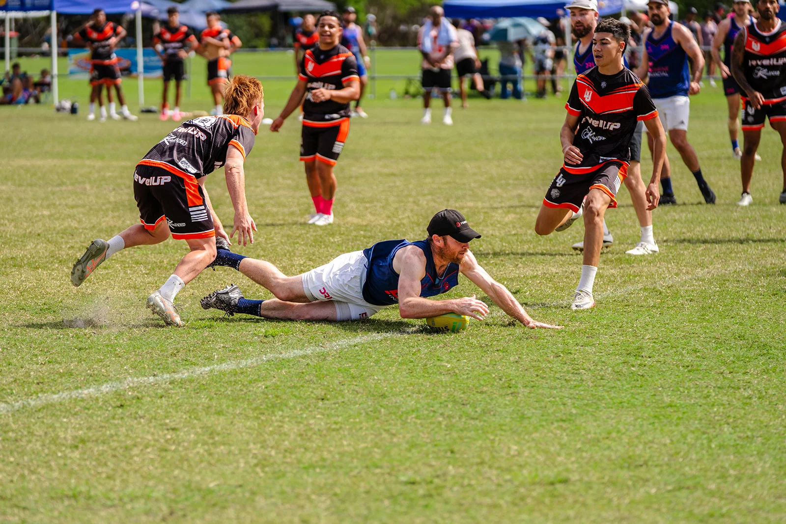 A player in white and blue dives across the grass ahead of red and black defenders.