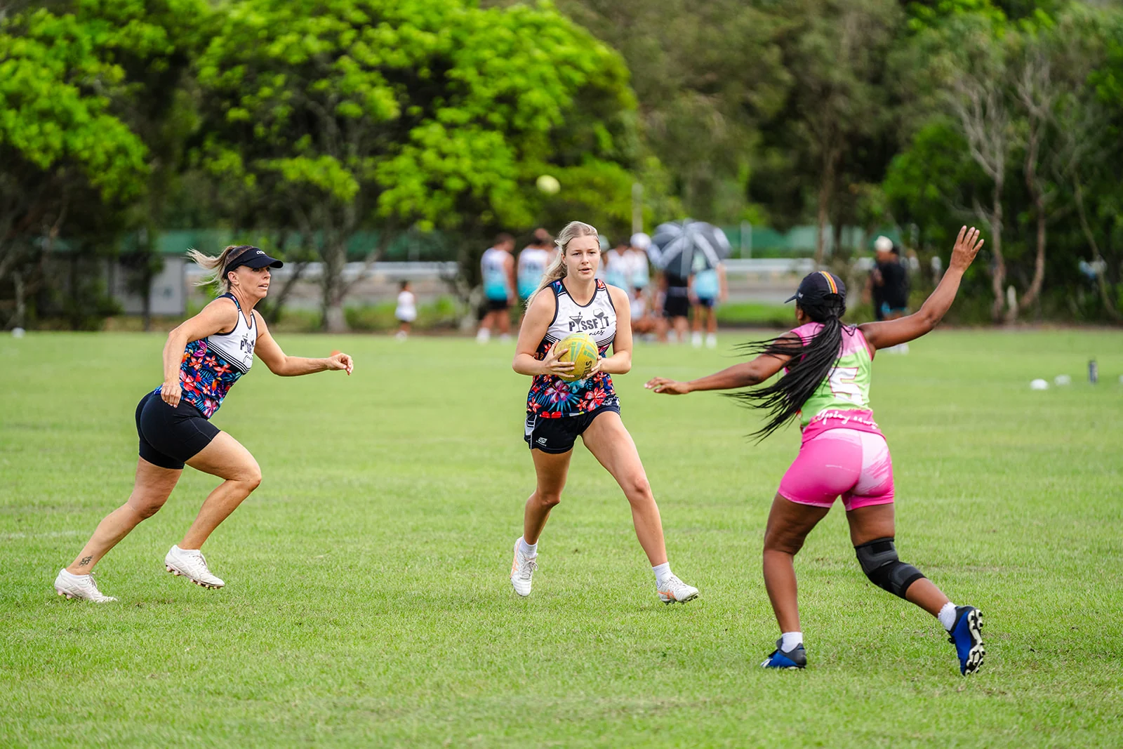 A woman in a floral kit changes direction with the ball between nearby players.
