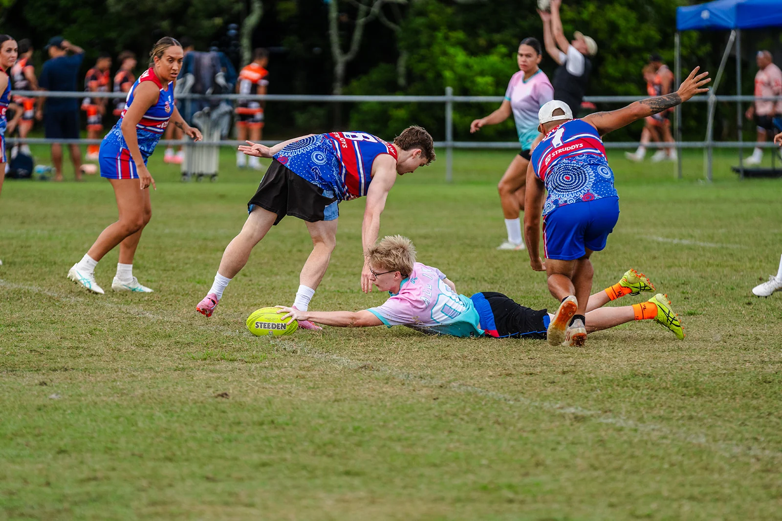 A player in pink and teal stretches flat along the ground with the ball.