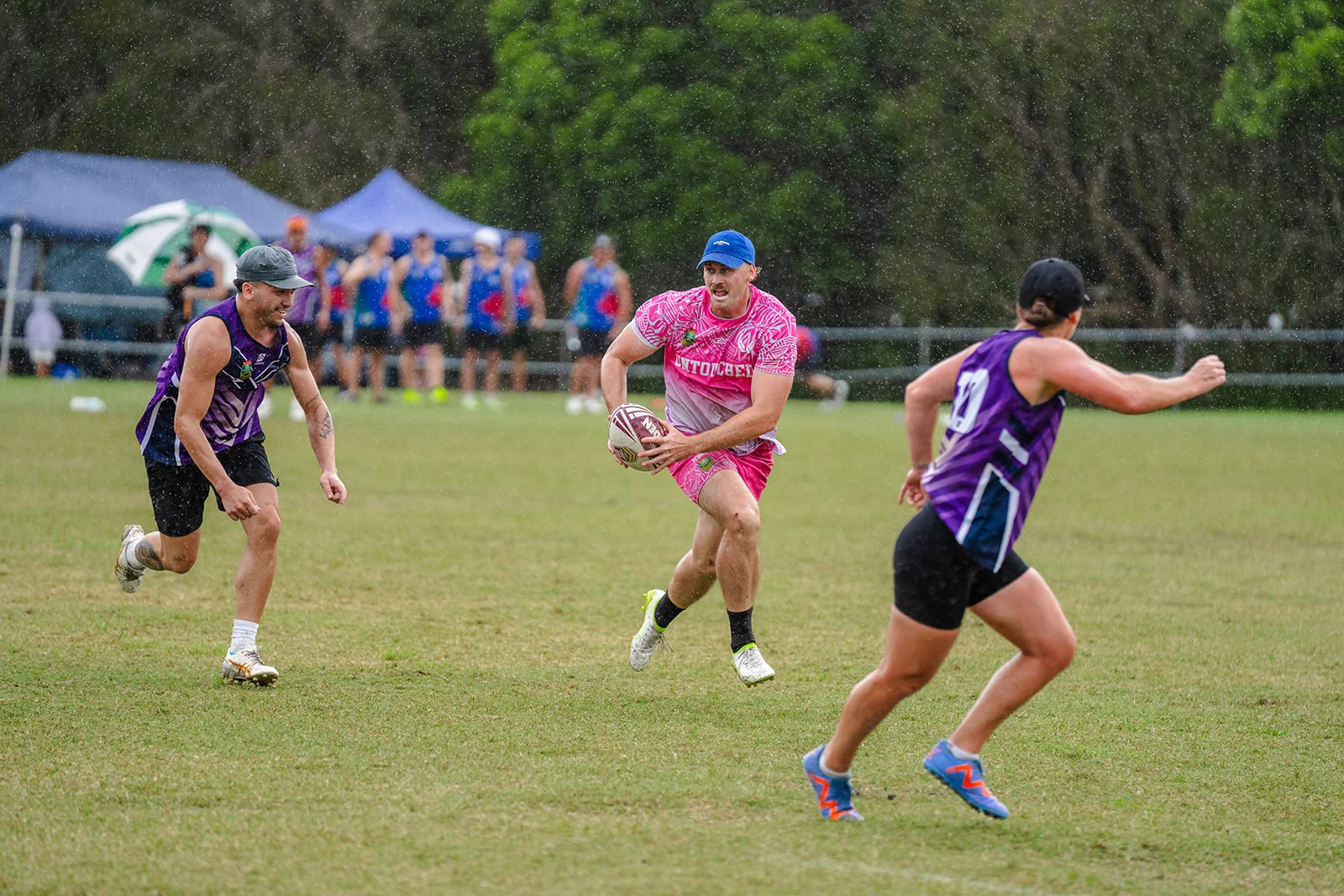 A player in pink pivots with the ball between purple defenders in the rain.