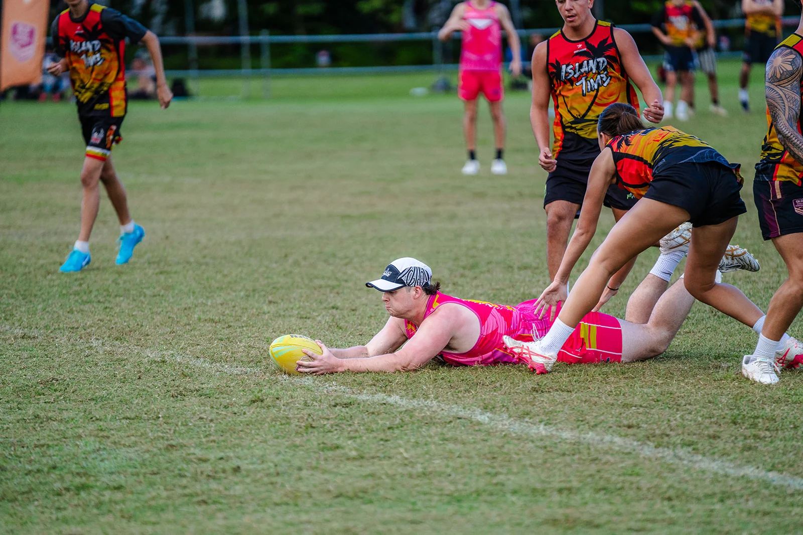A woman in pink stretches the ball forward along the grass beneath a defender.