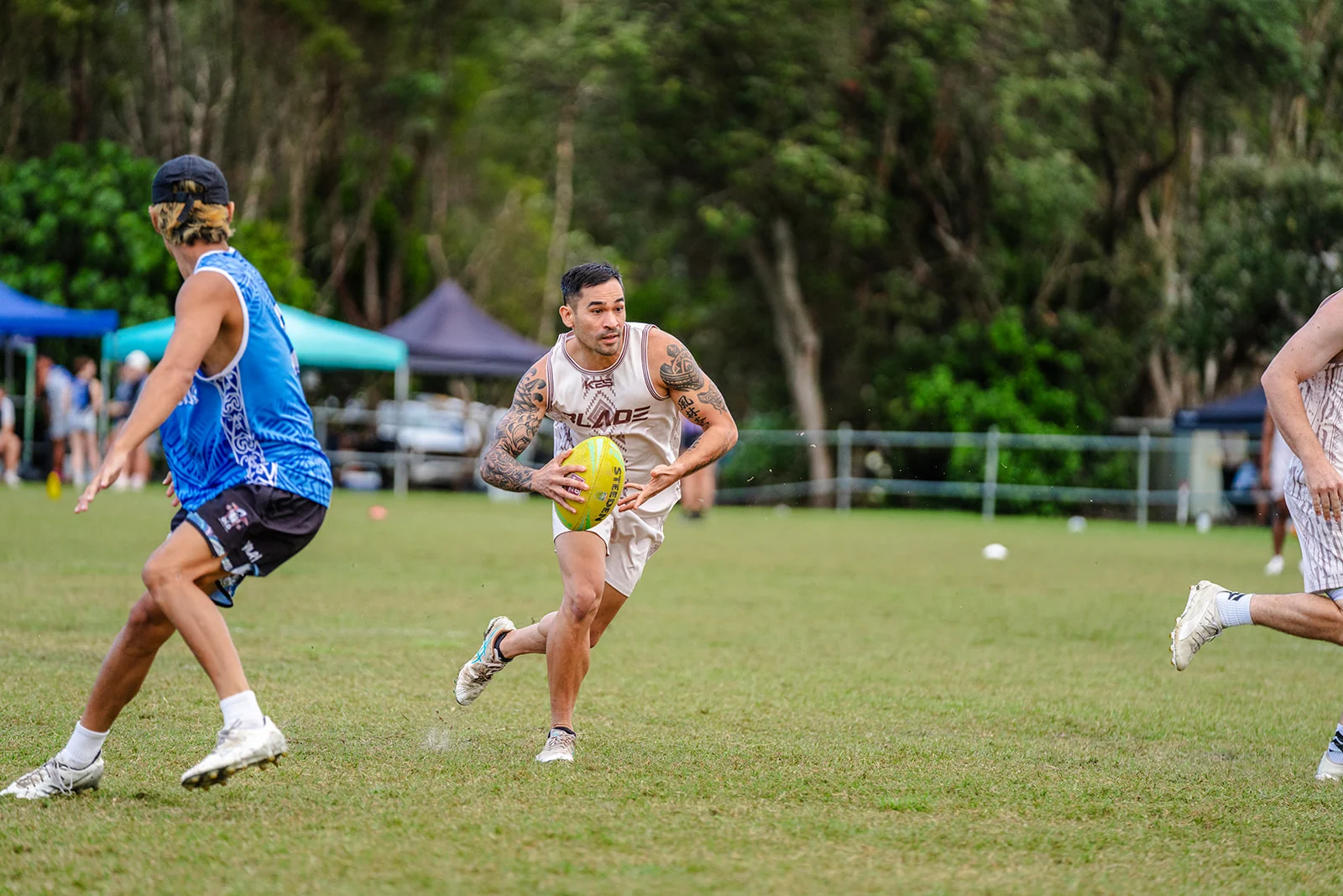 A tattooed ball carrier in white cuts across the field toward a blue defender.
