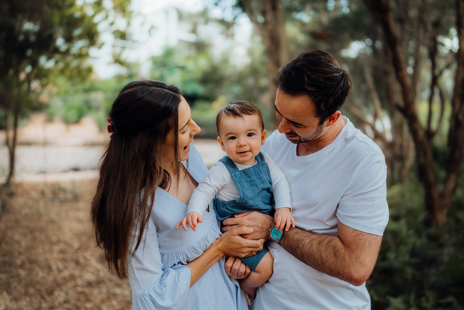 A smiling baby looks toward the camera while both parents look at him.