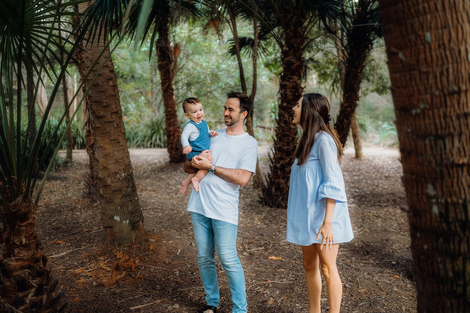 Parents walk together with their baby beneath the palms.