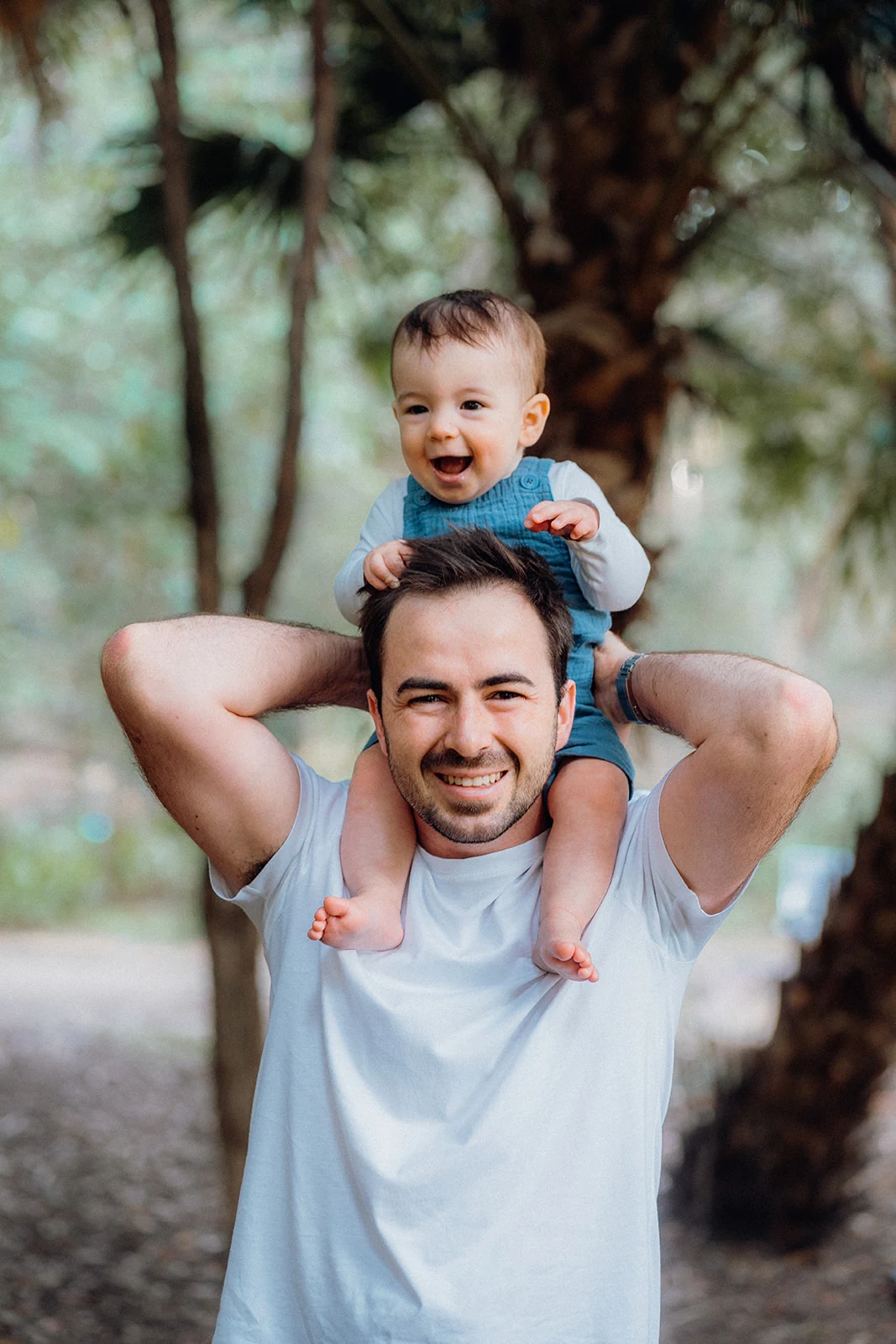 A smiling baby rides on his father’s shoulders.
