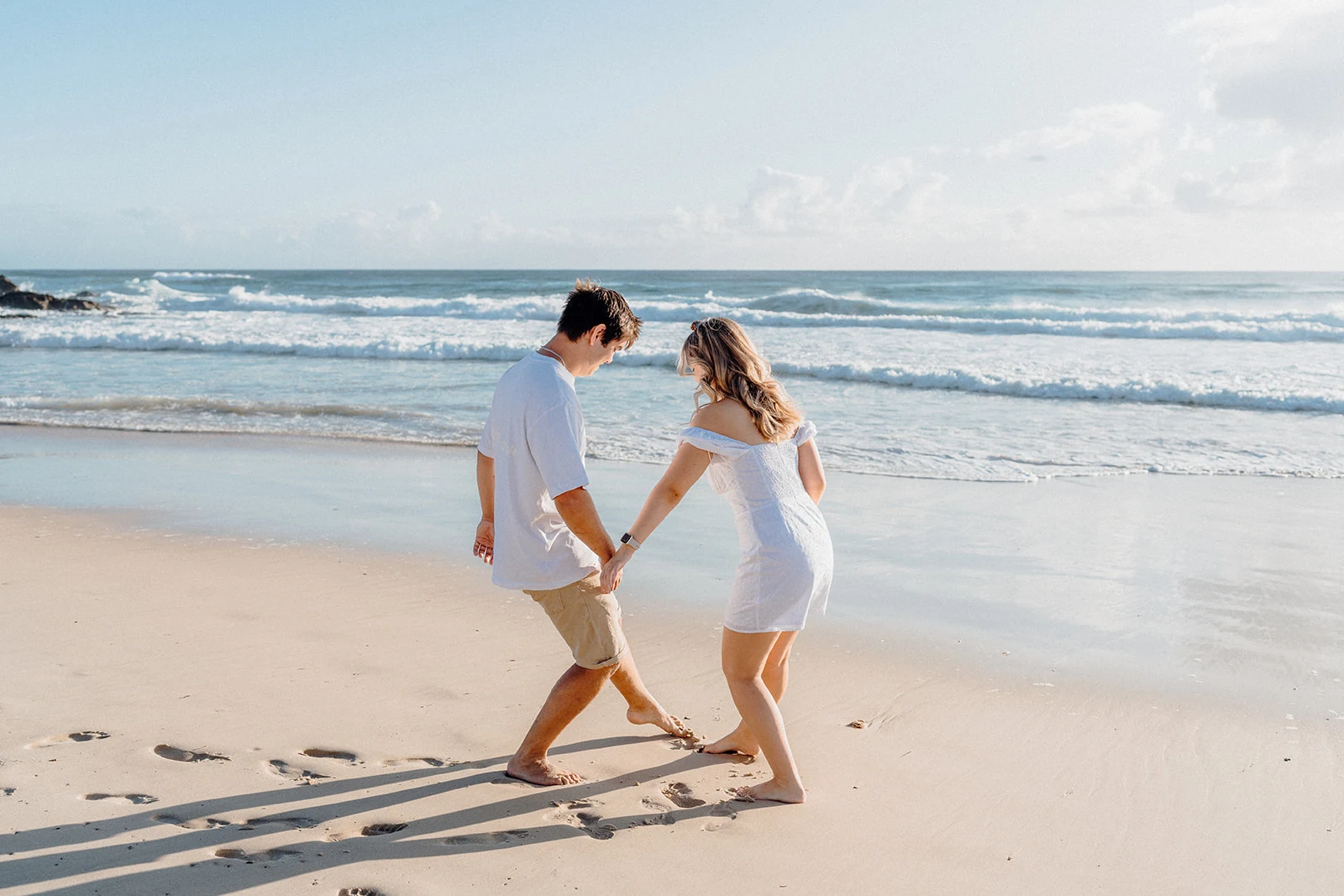 A couple holds hands while stepping across wet sand.