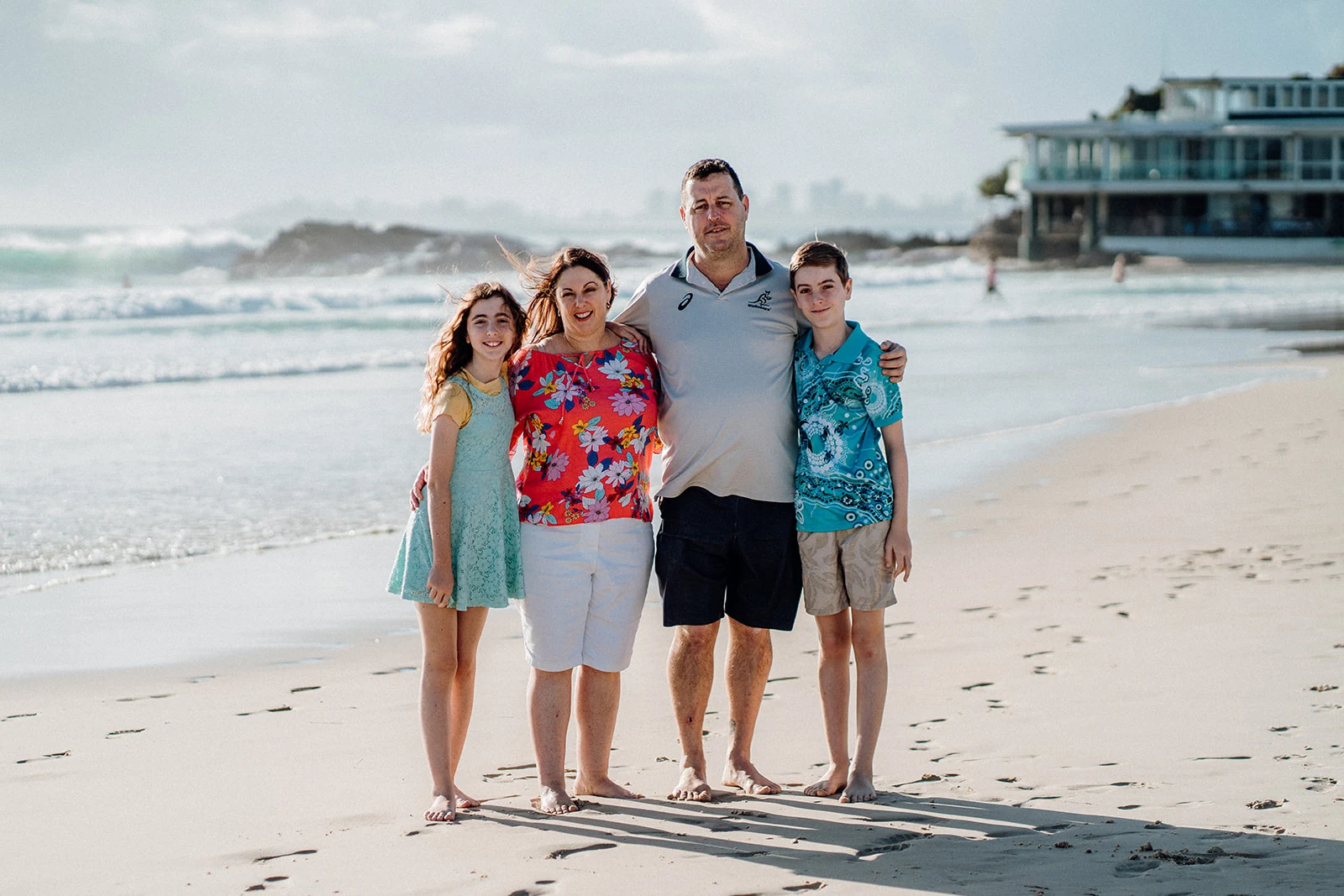 Parents and two children stand close together on the beach.