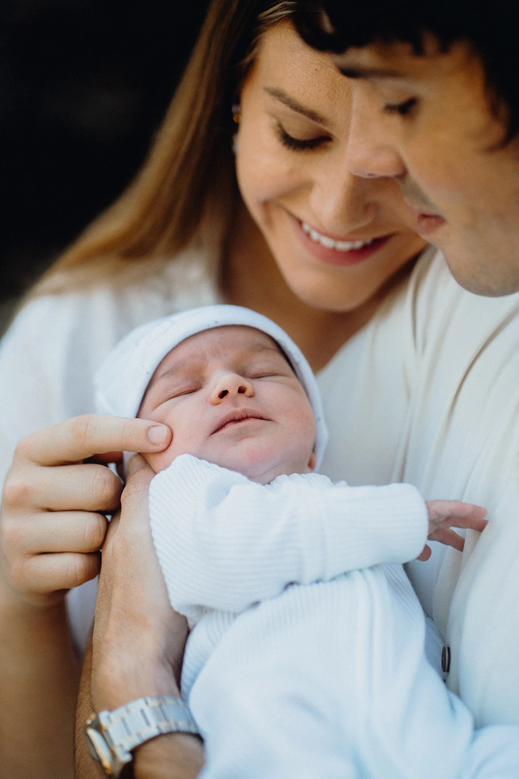 A close portrait of a sleeping newborn held beneath both parents’ smiling faces.