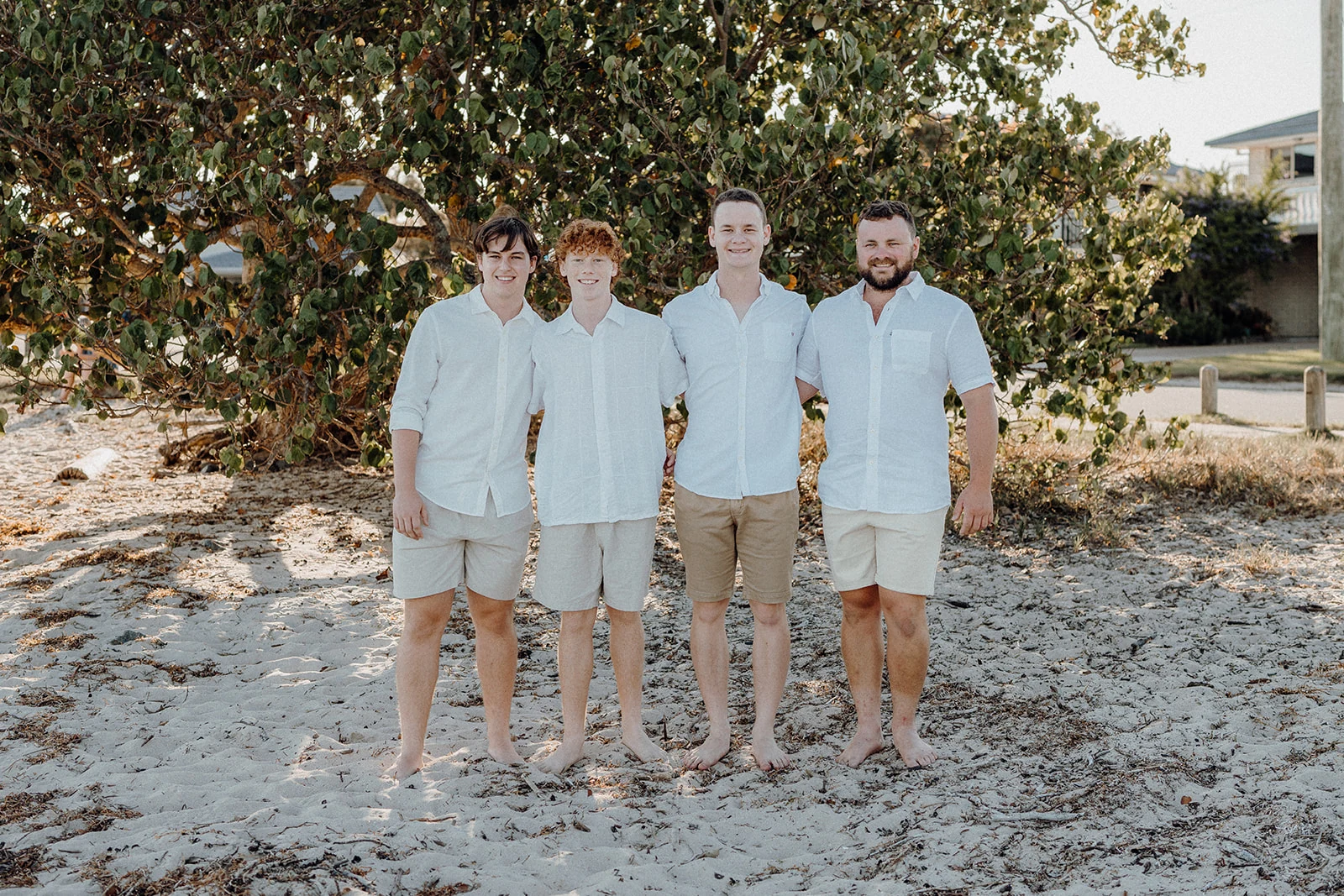 Four brothers stand together beneath a coastal tree.
