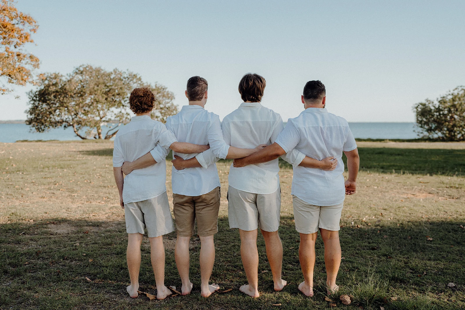 Four brothers stand with their arms around each other, facing the water.