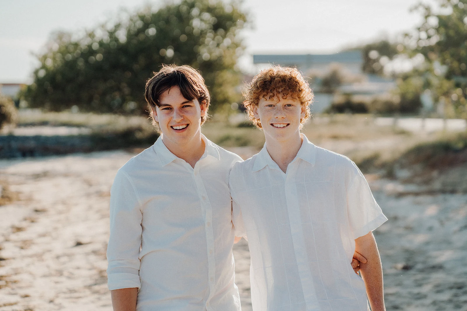 Two brothers smile together by the shore.