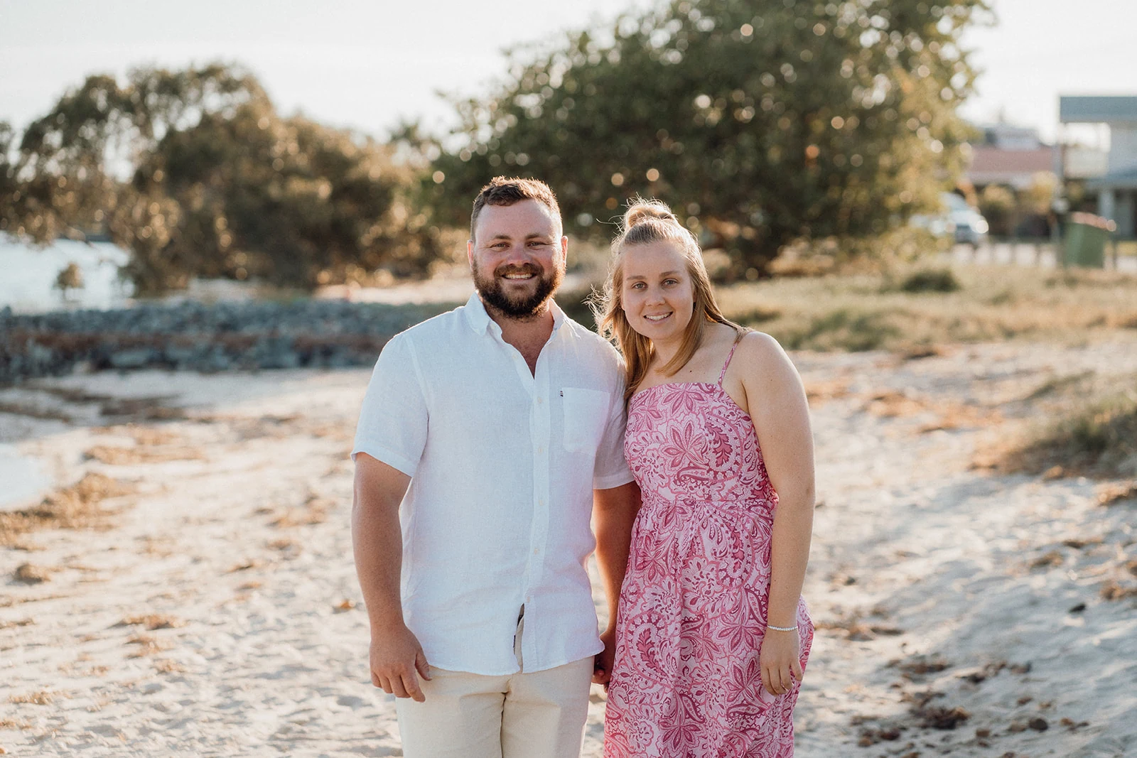 A couple stands together beside the water in warm evening light.