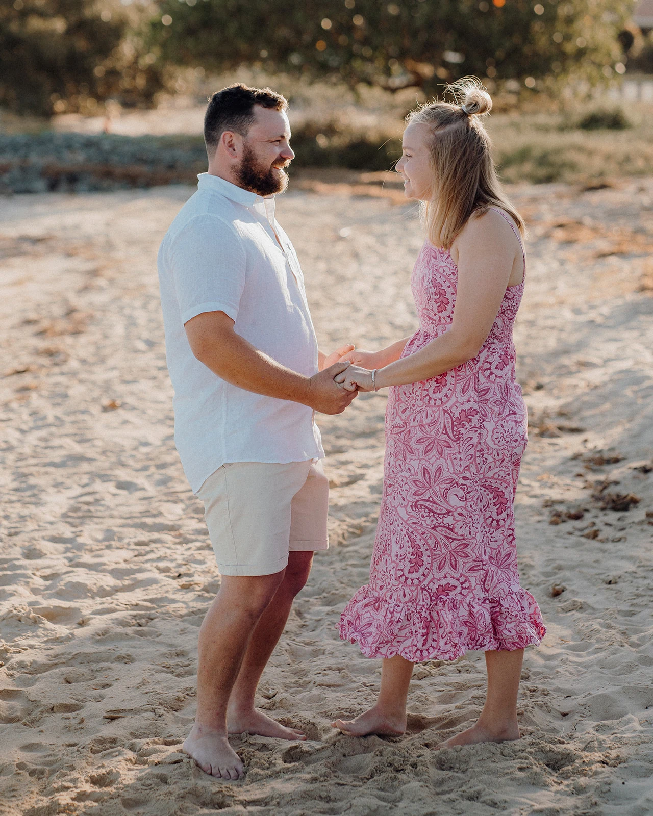A couple holds hands and smiles at each other on the beach.