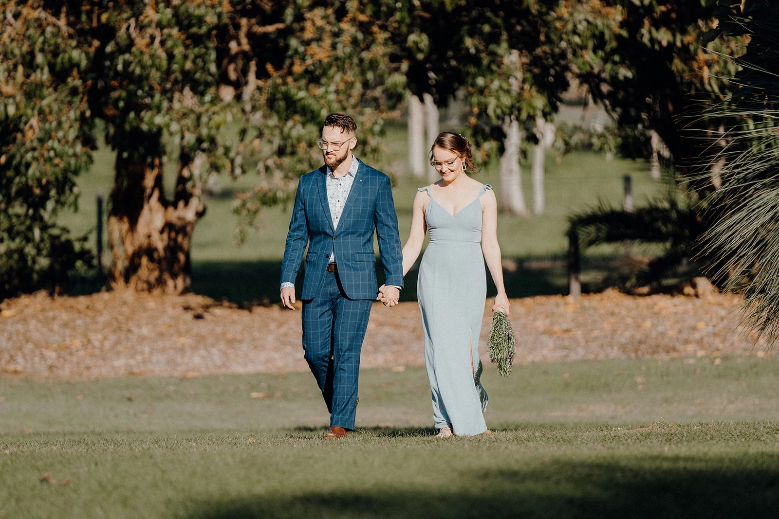 A couple walk hand in hand across a lawn toward their outdoor ceremony.