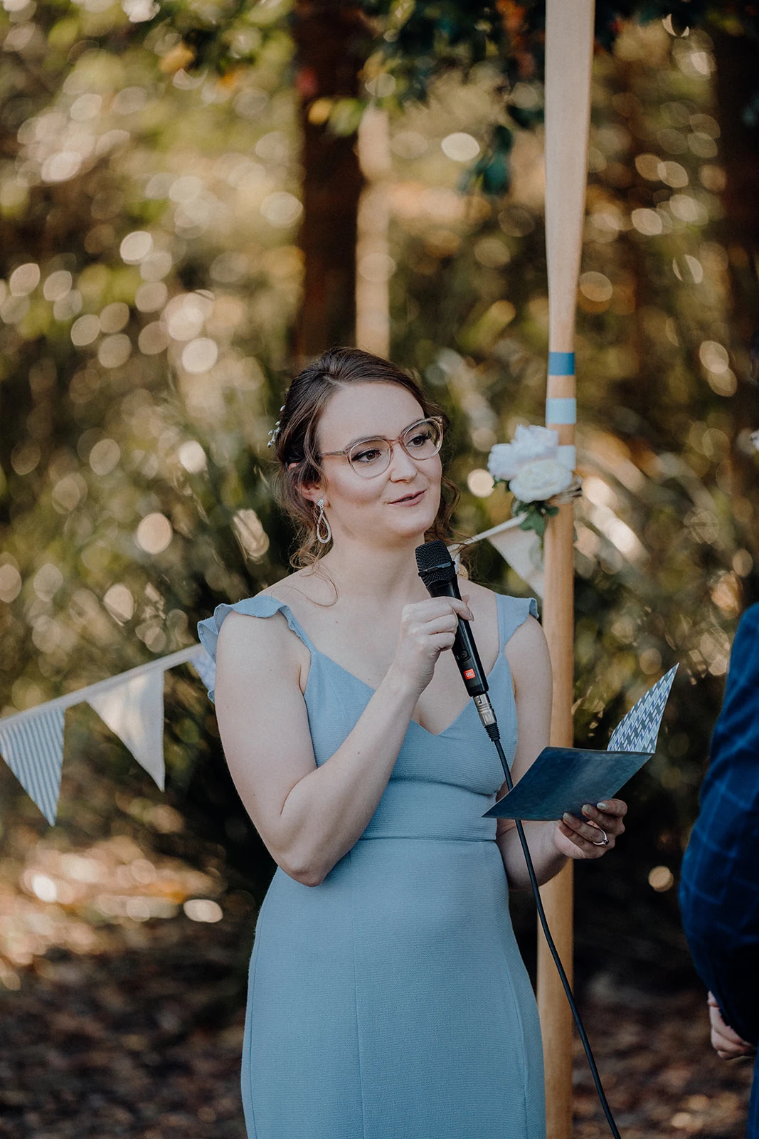 A bride reads her vows beneath trees and pale blue bunting.