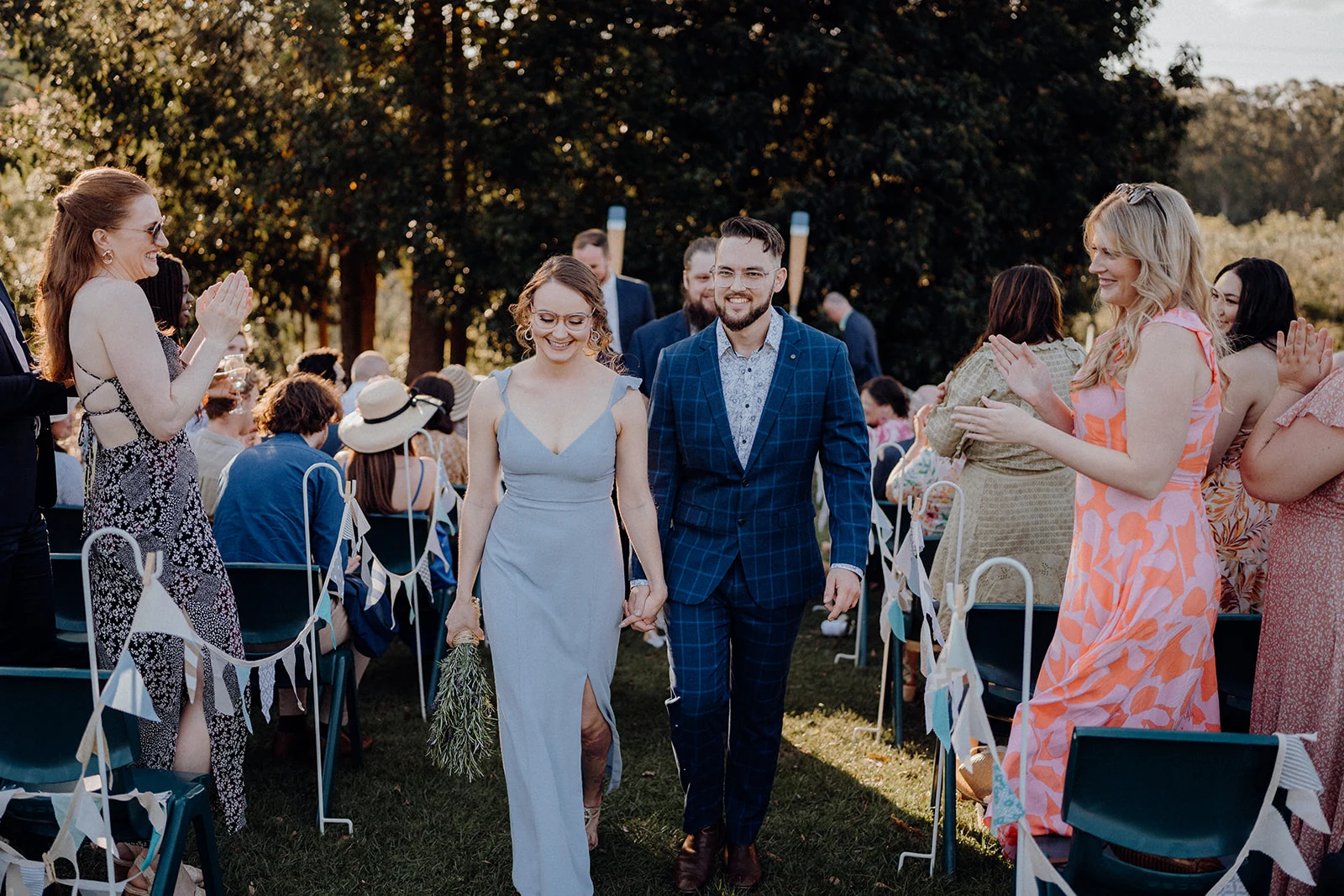 Newlyweds walk through smiling guests after their outdoor ceremony.
