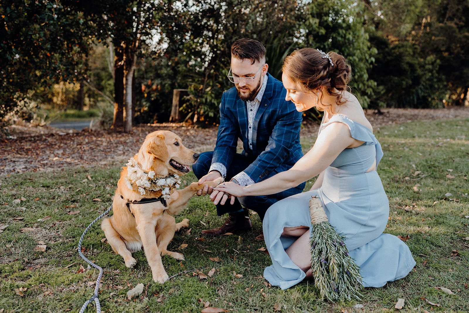 Newlyweds kneel beside their golden retriever and hold its paw.