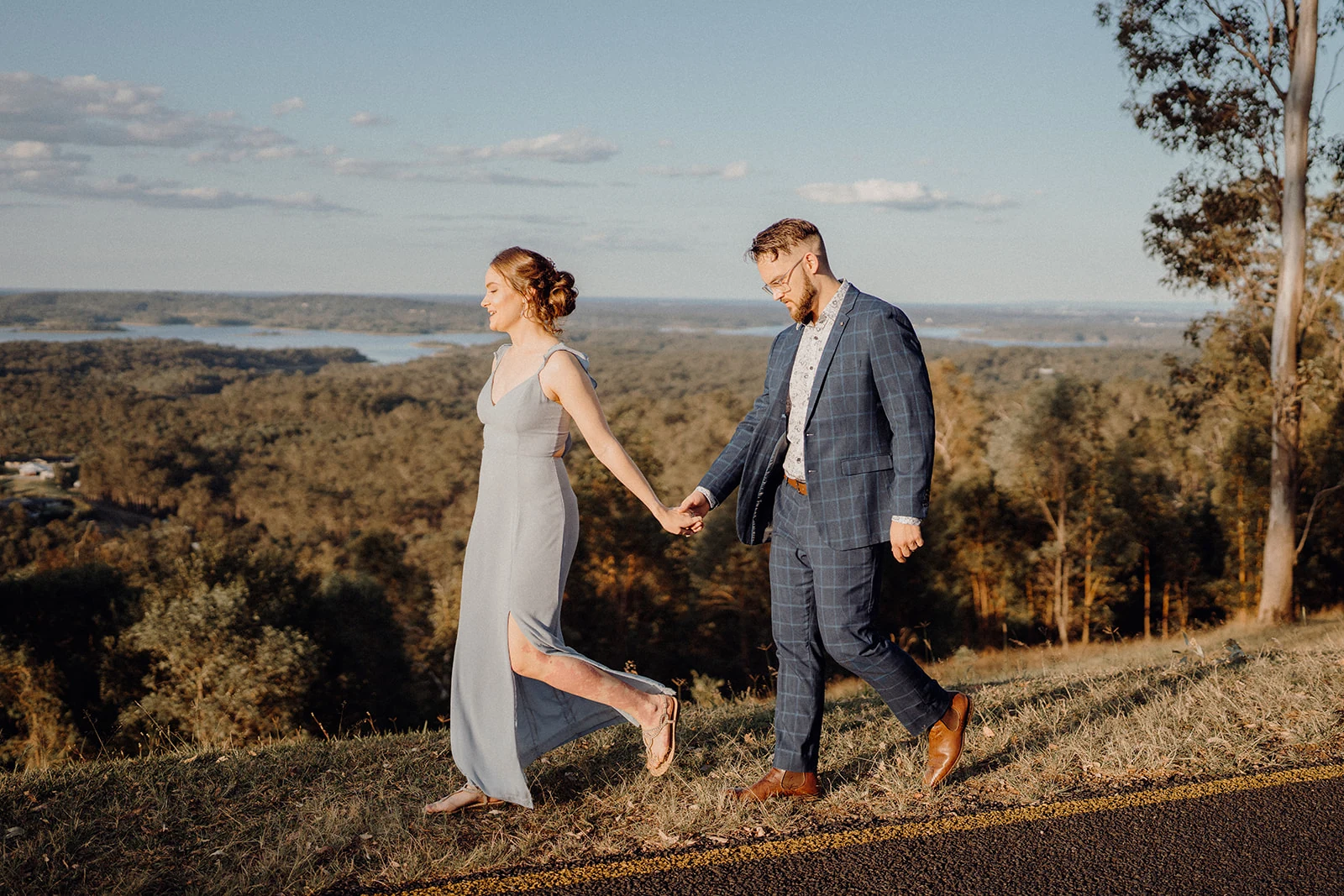 A couple walk hand in hand along a sunlit hilltop.