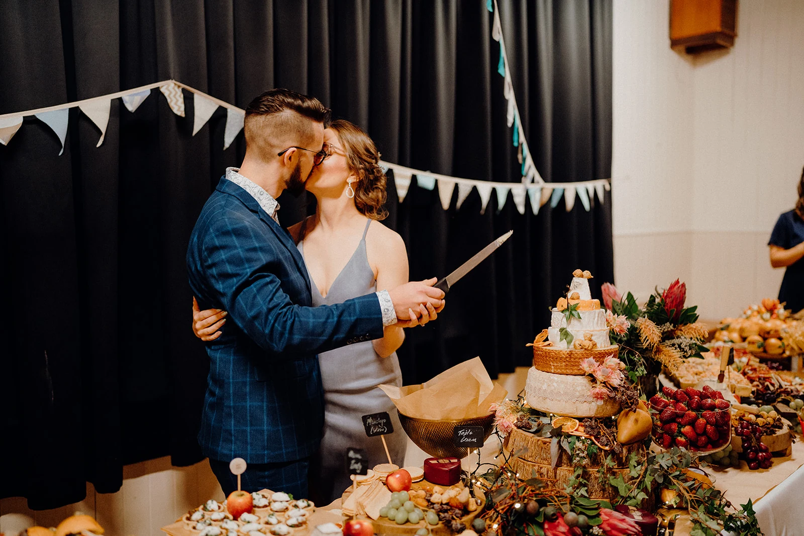 A couple share a kiss while cutting their wedding cake.