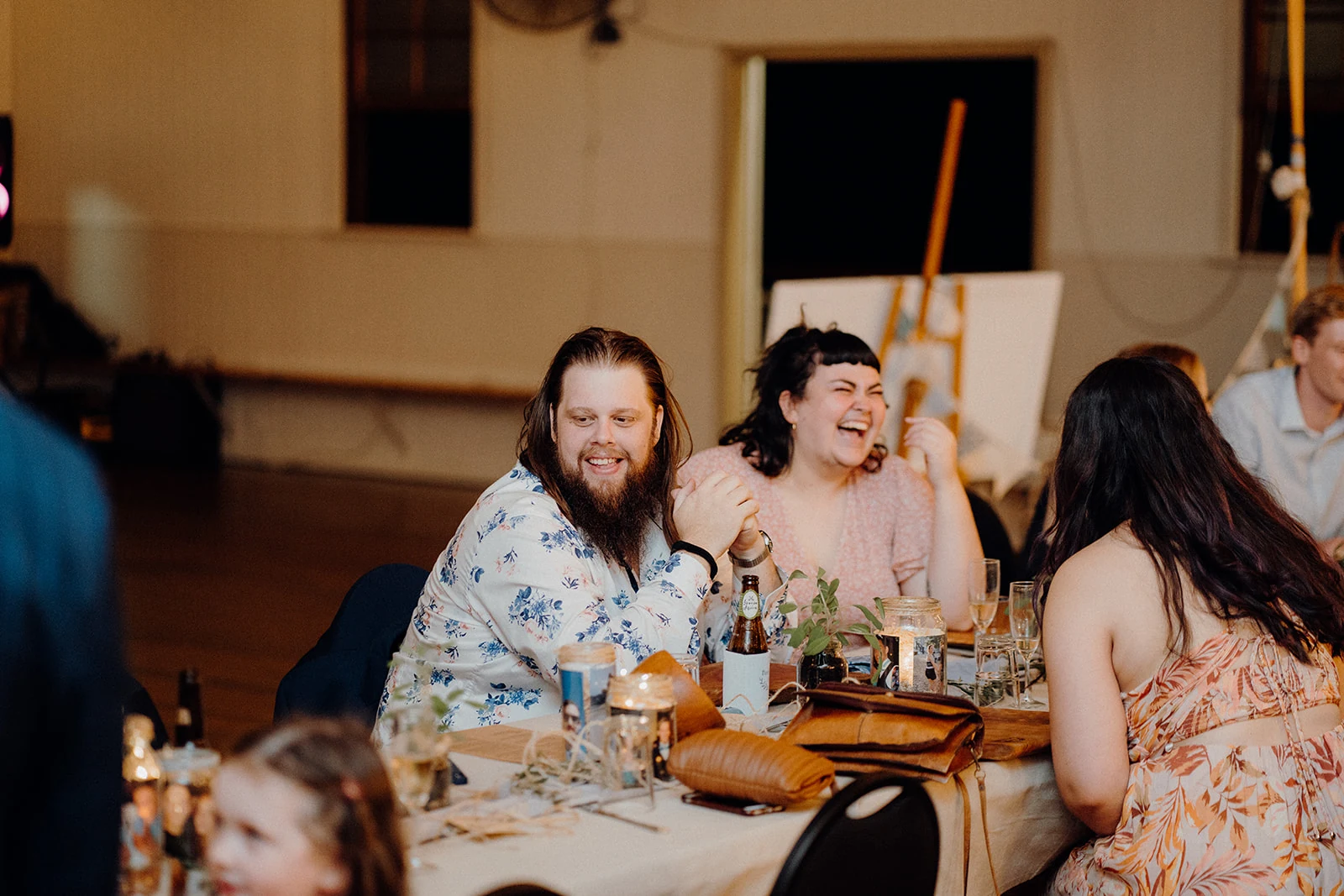 Wedding guests laugh together at a reception table.