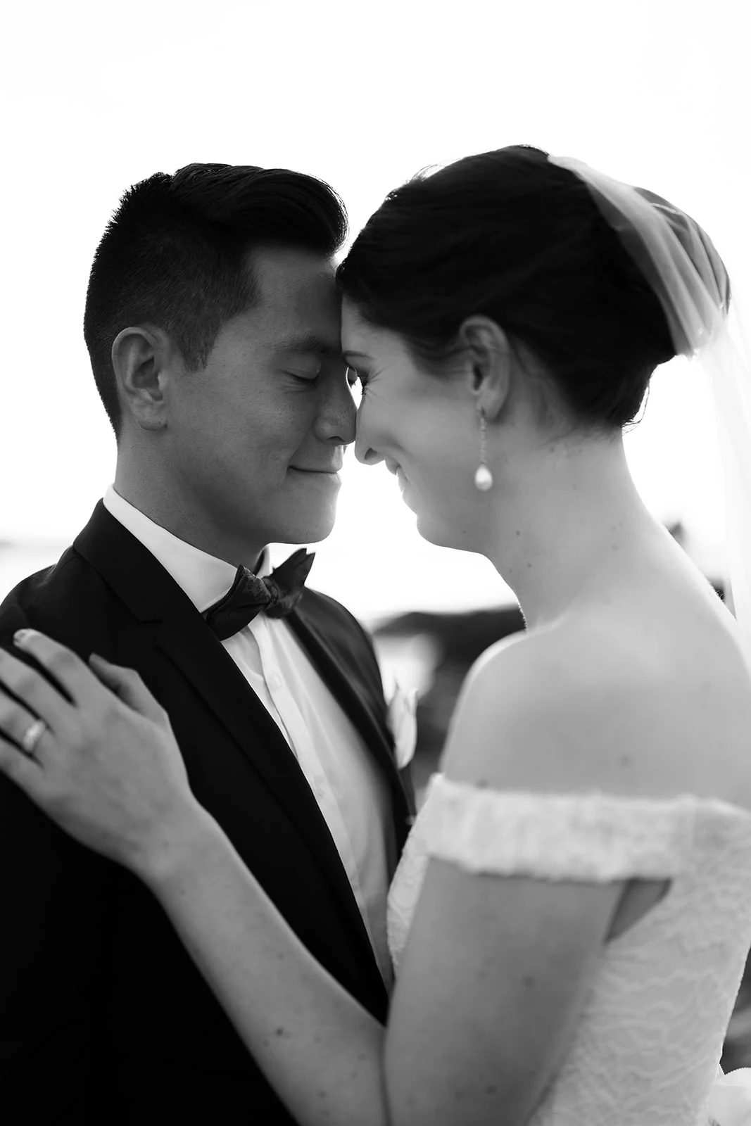 A bride and groom rest their foreheads together in a close black-and-white portrait.