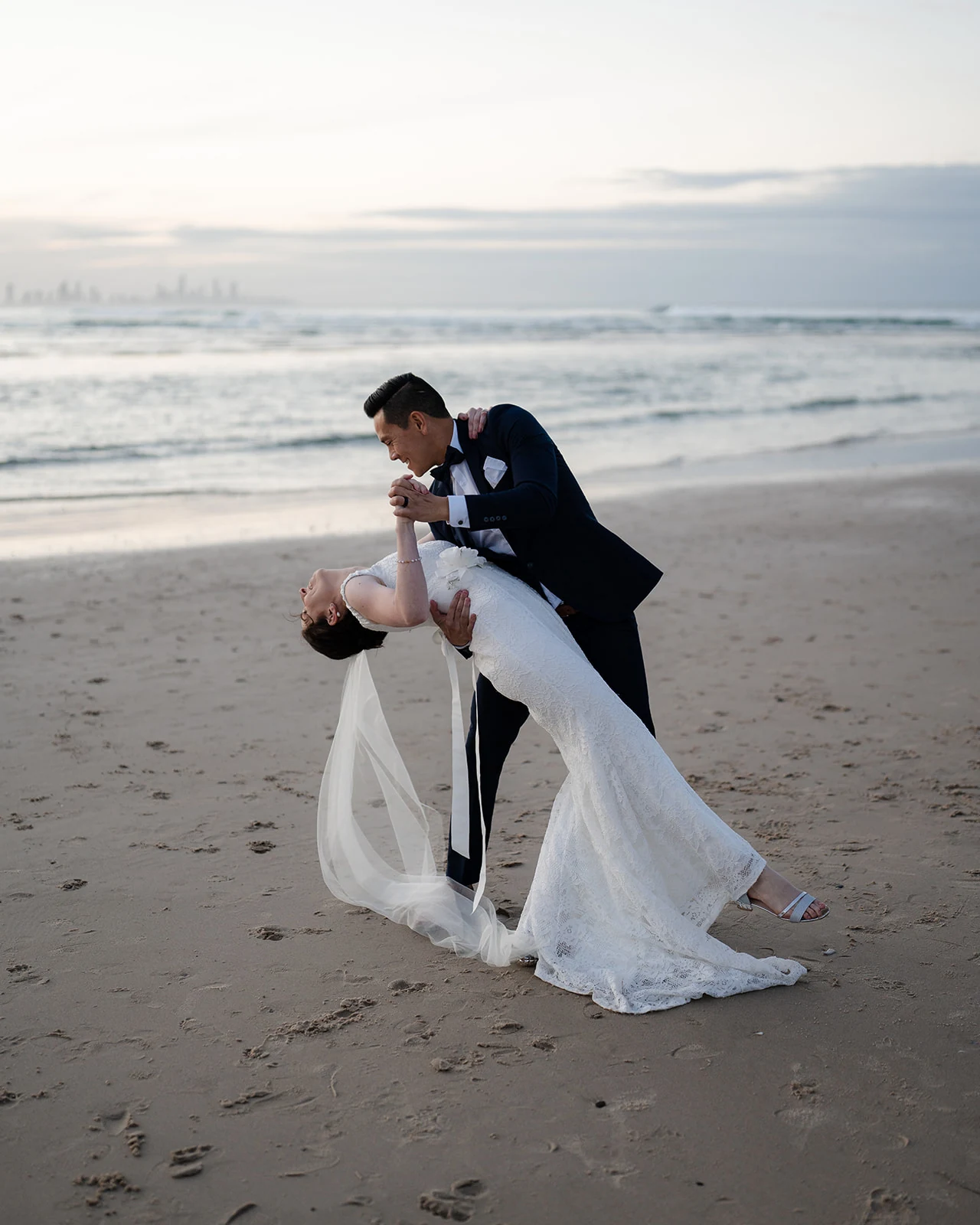 A groom dips his bride for a kiss on the beach.